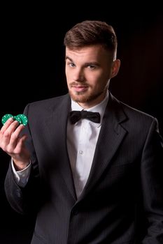 man in a suit posing with chips for gambling on black background