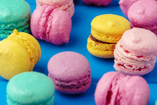 Pile of delicious colorful macarons on blue wooden background
