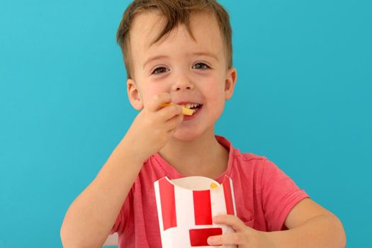 Young boy indoors eating fish and chips smiling blue background