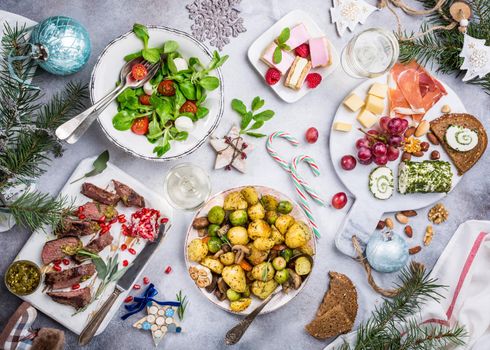 Flat lay of delicious Christmas themed dinner table with roasted meat steak, appetizers and desserts. Top view. Holiday concept.