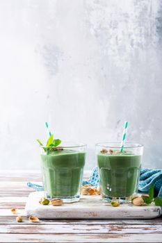 Two glasses of healthy green smoothie with mint, pistachios and spirulina on old wooden background. Detox, diet, healthy, vegetarian food concept with copy space.