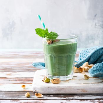 Healthy green smoothie with mint, pistachios and spirulina in glass on old wooden background. Detox, diet, healthy, vegetarian food concept with copy space.