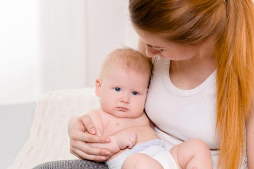 Mother and child on a white bed. Mom and baby girl in diaper playing in sunny bedroom. Parent and little kid relaxing at home. Family having fun together. Bedding and textile for infant nursery.