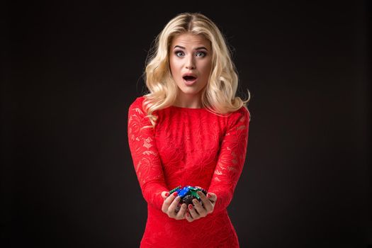 Young emotional woman holding a bunch of chips in her hands on a black background. Poker