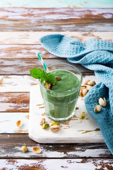Glass of healthy green pistachio smoothie spirulina on old wooden background. Detox, diet, healthy, vegetarian food concept with copy space.