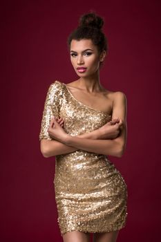 Fashion young African woman with make-up, in short sexy gold dress. Model on a claret background in the studio