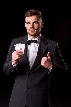 man in a suit posing with cards for gambling on black background