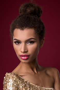 Fashion young African woman with make-up, in sexy gold dress. Model on a claret background in the studio