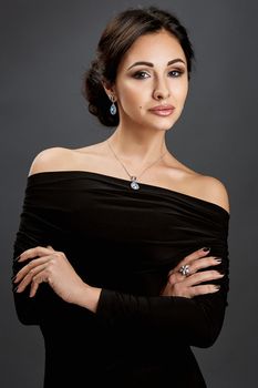 Beautiful woman standing in a black dress over gray background. Woman looking at the camera