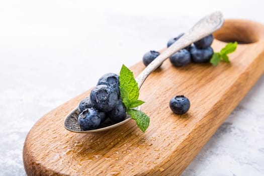 Fresh blueberries in vintage spoon on wooden cutting board. Healthy eating and nutrition concept with copy space.