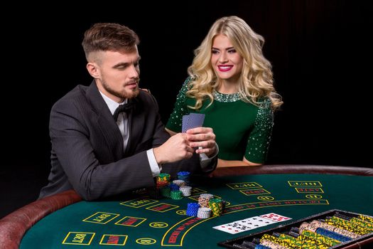 couple playing poker at the green table. The blonde girl and a guy in a suit.