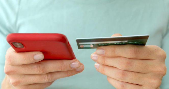 Close-up woman's hands holding a credit card and using cell phone for online shopping