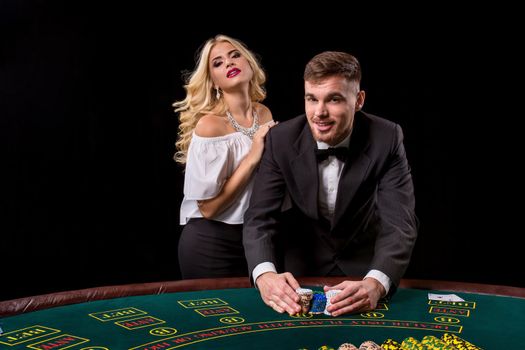 View of young, confident, man with the lady while he's playing poker game. They both look at the camera and smiling
