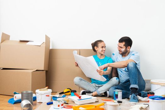 Couple discussing home redesign ideas. Man and woman together planning new home interior design. Cardboard boxes, painting tools and materials on floor. House remodeling and architectural renovation.