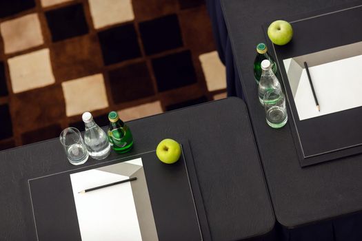 Top view of black tables in classroom ready for testing with water bottles and apples next to paper and pencil