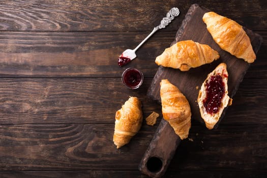 Delicious fresh mini croissants with fruit jam on wooden cutting board on old dark background. Healthy Breakfast with copy space. Top view.