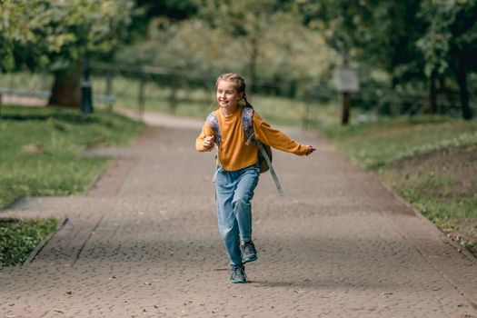 Pretty school girl with backpack running in the park after lessons. Sweet child kid at autumn outdoors