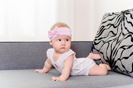 Portrait of a baby girl with a bandage and a bow on her head on a sofa. Beautiful child with blue eyes