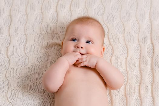 Happy baby lying on a white plaid in the bedroom. Sweet baby in a diaper