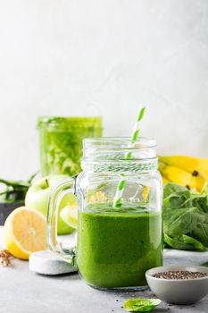 Healthy green smoothie with spinach, banana, lemon, apple and chia seeds in glass jar and ingredients. Detox, diet, healthy, vegetarian food concept with copy space.