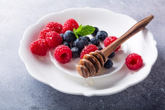 Freshly blueberries and raspberries on white plate with honey. Healthy eating and nutrition concept with copy space.