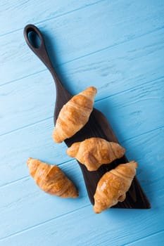 Delicious fresh mini croissants on wooden cutting board on blue background. Healthy Breakfast with copy space. Top view.