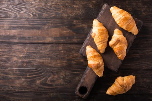 Delicious fresh mini croissants on wooden cutting board on old dark background. Healthy Breakfast with copy space. Top view.