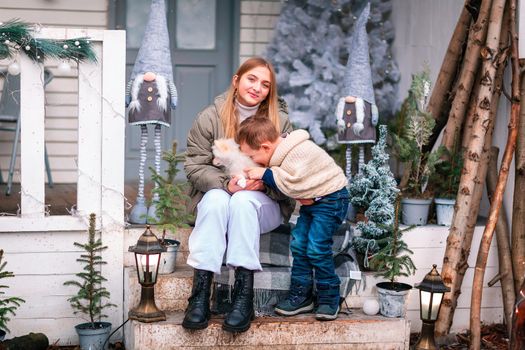 Happy little kids with white little puppy sitting on the porch of the Christmas decorated house, snowing outdoor. Happy New Year and Merry Christmas. Magic winter