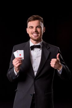 man in a suit posing with cards for gambling on black background