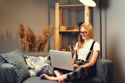 Young woman working on laptop at home, sitting on the sofa.