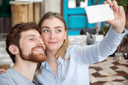 Content man and woman posing for selfie using smarpthone.