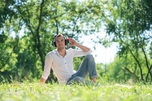 Young man in the park listens to music. He sits on the grass and enjoys music.