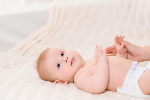 Happy baby lying on a white plaid in the bedroom. Sweet baby in a diaper