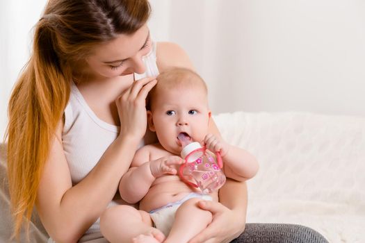 Mother and child on a white bed. Mom and baby girl in diaper playing in sunny bedroom. Parent and little kid relaxing at home. Family having fun together. Bedding and textile for infant nursery.