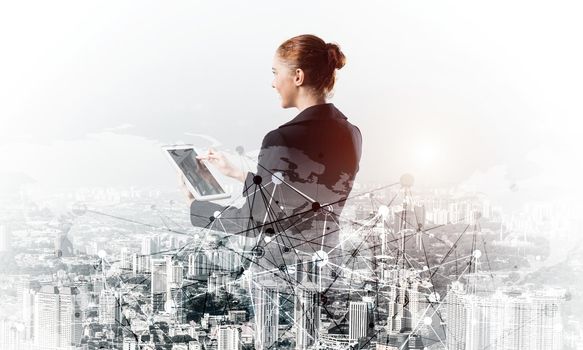 Young businesswoman using tablet computer. Double exposure concept with modern cityscape and beautiful woman in business suit. Digital technology in property management and development company.