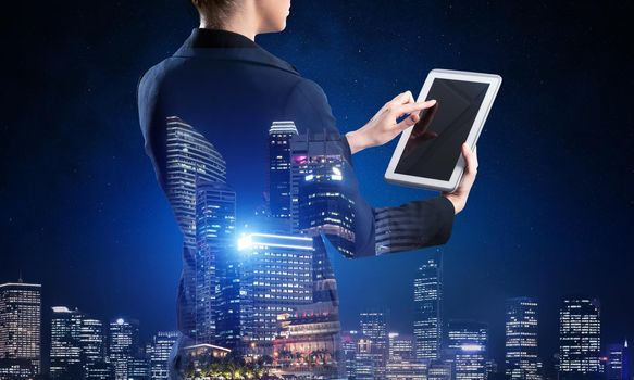 Businesswoman using tablet computer. Double exposure concept with night city and woman in business suit. Real estate investment and development. Digital technology in strategy planning and management.