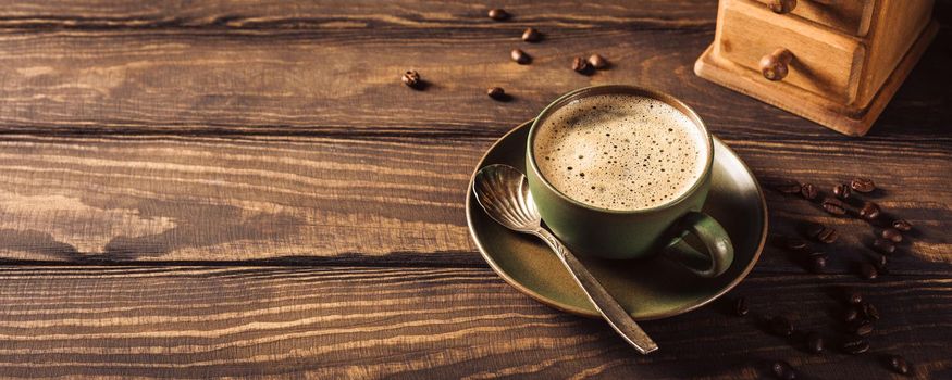 Wooden background with green cup of coffee, beans and coffee grinder. Copy space. Retro style toned dark photo. Banner.