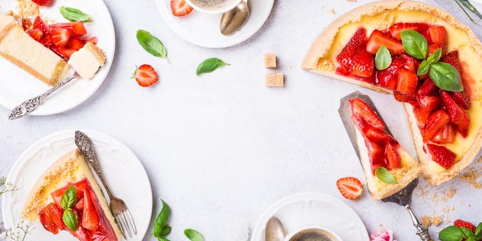 Overhead shot of cups of coffee, delicious homemade strawberry cheesecake and flowers on light gray background. Top view, flat lay. Copy space.