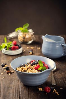 Oat granola with berries and yoghurt in blue bowl on dark old wooden background. Copy space. Healthy breakfast concept.