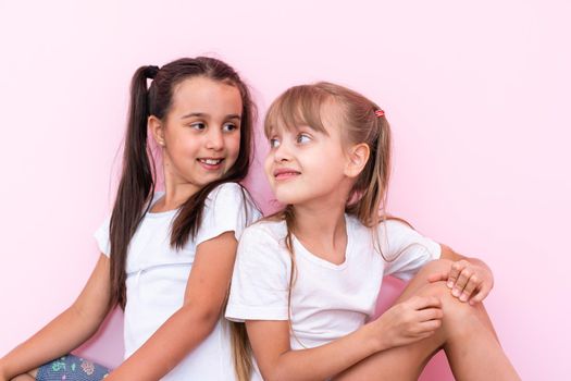 two little girl sitting on floor and looking up. Isolated on a pink background