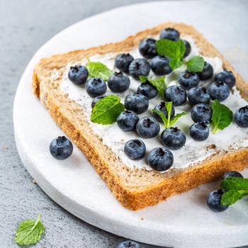 Delicious open sandwich with goat cheese and blueberries for breakfast or lunch on marble board. Food background.