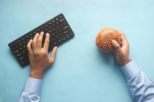 young man typing on keyboard while holding a burger ,