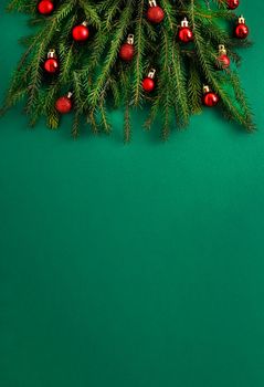 Christmas tree made of green coniferous branches on a green background. Christmas background with place for text. Christmas holiday concept. Ball toys. Red balls