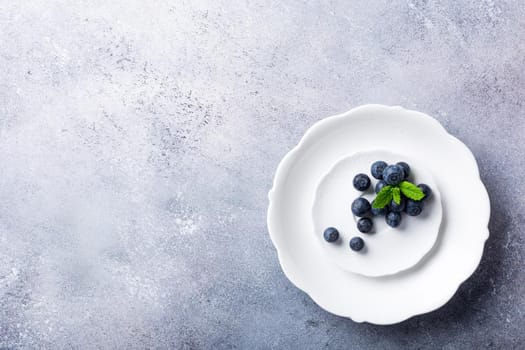 Freshly picked blueberries on white plate on gray stone background. Concept for healthy eating and nutrition with copy space. Top view.