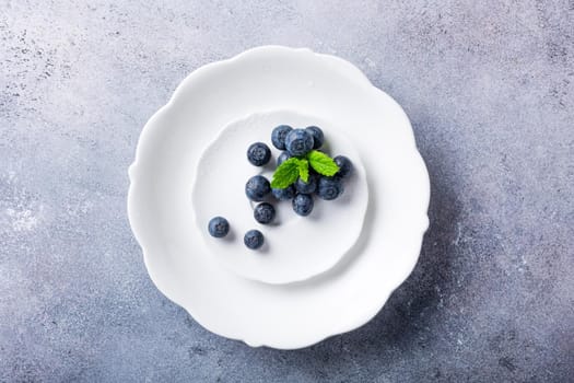 Freshly picked blueberries on white plate on gray stone background. Concept for healthy eating and nutrition with copy space. Top view.