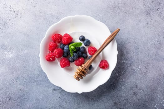 Freshly blueberries and raspberries on white plate with honey. Healthy eating and nutrition concept with copy space. Top view.