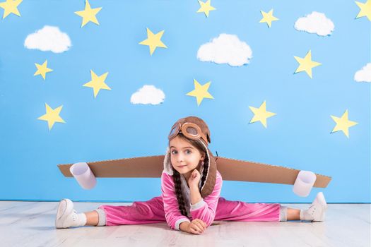 Girl pilot playing with toy jet pack at home. Success and leader concept. Kid on the background of bright blue wall with white clouds and yellow stars.