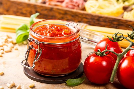 Glass jar with homemade classic spicy tomato pasta or pizza sauce with pine nuts and basil. Italian healthy food background.