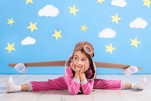 Girl pilot playing with toy jet pack at home. Success and leader concept. Kid on the background of bright blue wall with white clouds and yellow stars.