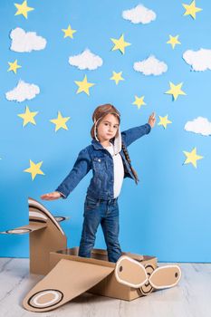 Little child girl in a pilot's costume is playing and dreaming of flying over the clouds. Portrait of funny kid on a background of bright blue wall with yellow stars and white clouds